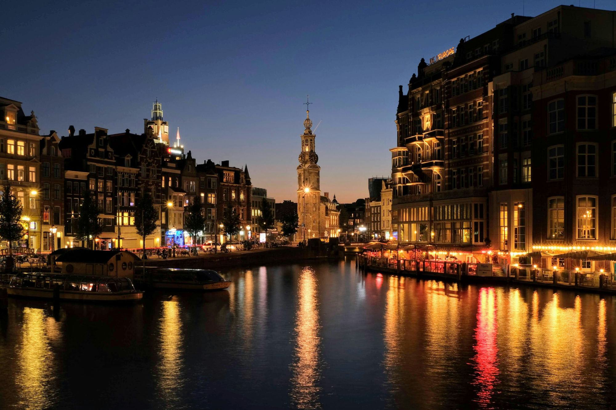 De Munttoren aan de Amstel in Amsterdam bij avondlicht, met verlichte grachtenpanden en weerspiegelingen in het water
